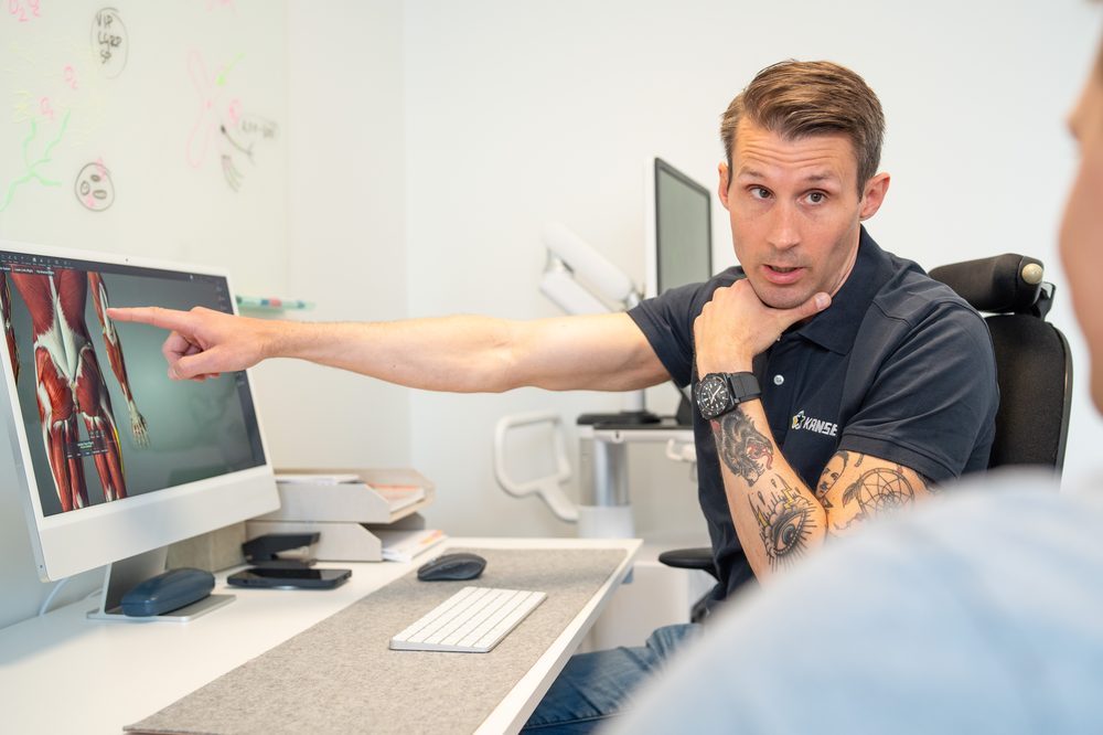 Carl-Robert Kårell pekar på en anatomisk bild på skärmen och förklarar för en patient